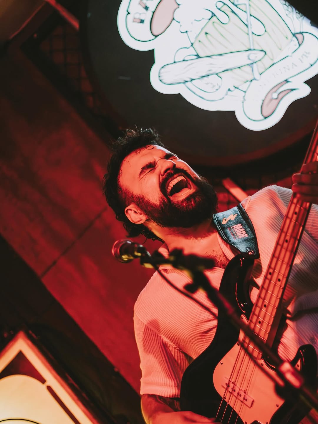 Lugue Henriques playing bass mid-song under red stage light, head thrown back.