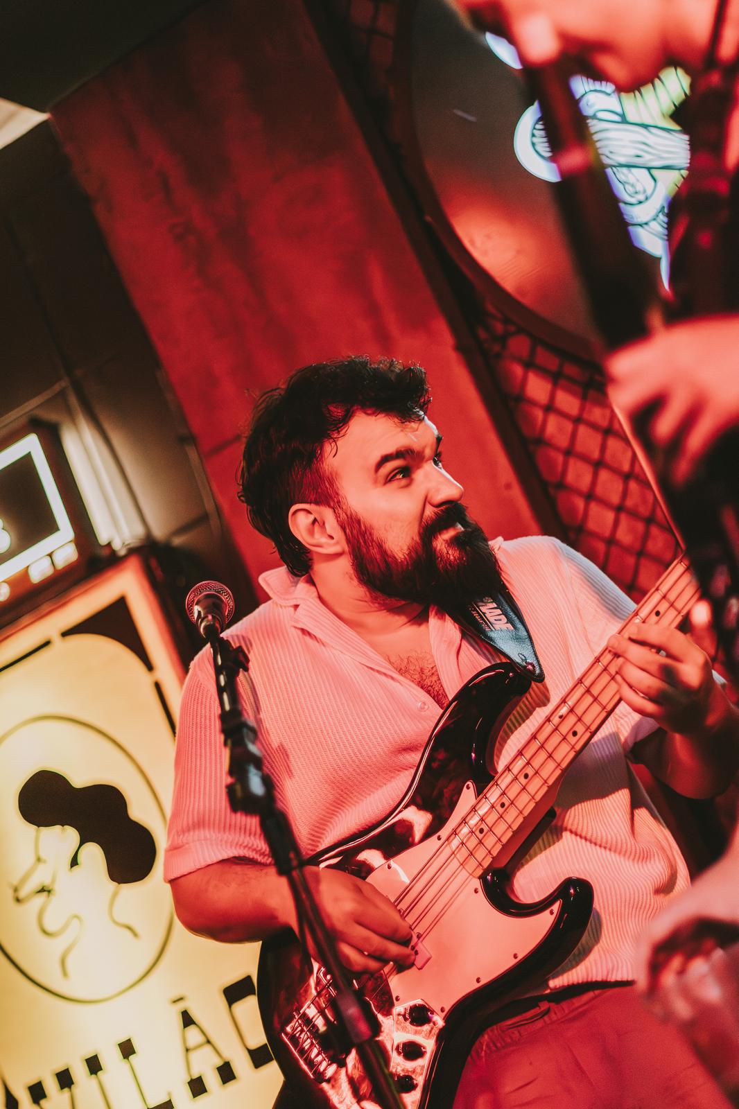 Portrait of Lugue Henriques looking down at his bass on stage in warm red light.